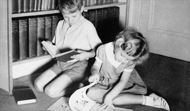 photograph showing a young boy and girl seated reading books. 1955