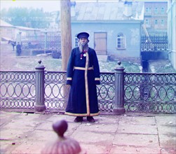 Russian man against a village backdrop; by Sergey Mikhaylovich Prokudin-Gorskii