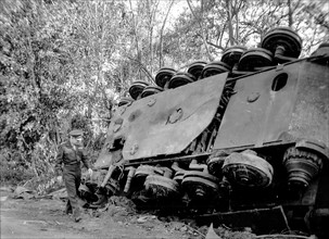 General Eisenhower walks past a destroyed tank.