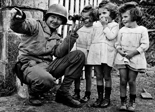 Soldier holding binoculars up to three little girls.