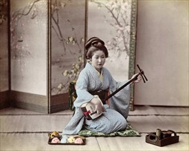 Colour photograph of a Japanese woman playing a samisen