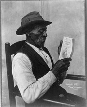 African American man seated and looking at magazine 'Harper's Ferry'