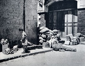 Photograph of an Arab soldier guarding a road block in the Old City in Jerusalem, whilst a young boy searches through the rubble