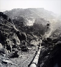 Photograph of helicopter transporting a bag of wet cement to be used in construction in a isolated mountainous area of California
