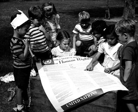 Photograph taken of children of the United Nations International Nursery School looking at a poster of the Universal Declaration of Human Rights