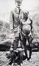 Photograph of a member of a pigmy tribe, standing with a European visitor