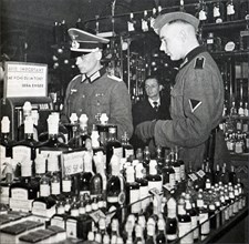 A German officer and soldier browse through a shop of bottles of wine and alcohol in Paris during World War II