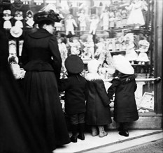Weihnachten 1902 - Kinder stehen mit ihrer Mutter vor einem Schaufenster mit Puppen