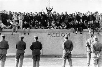 Germany / GDR Berlin: The fall of the wall. People on the wall. In front of them Vopos (border guards).