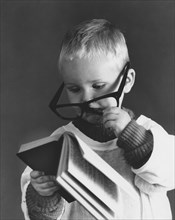 Little boy with big glasses reading a book in full concentration