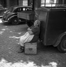 Woman sitting on a wooden box and leaning against a car