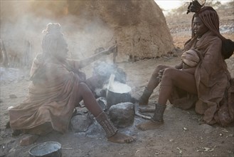 Two hang-girls cooking in front of a mud hut by the fire