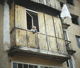 Young boy looks out of the window of an almost deserted house