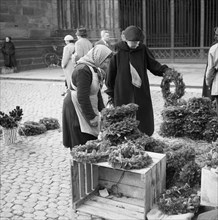 Woman inspects the goods at a market stall with Christmas wreaths