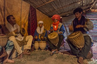 Bedouins with traditional clothes play on drums in a tent