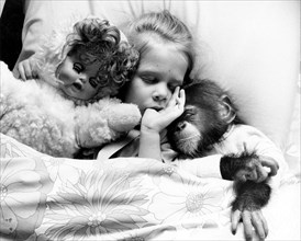 Girl in bed with chimpanzees and dolls