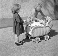 Two children play with a doll in a pram
