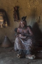 Woman of the people of Ovahimba or Himba suckling toddler in a hut