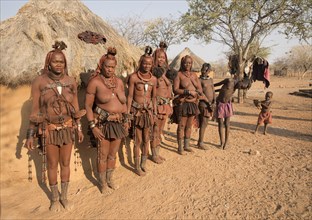 Himba women with children in front of a sleeping hut