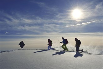 Three snowshoe walkers run in the snow against the light