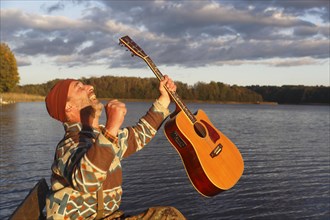 Man plays guitar on a boat landing stage at the lake and is pleased