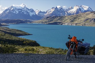 A heavily packed motorcycle on a gravel road behind the Lago del Torro and the mountain group Cordillera Paine
