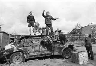 Three children play with car wreckage