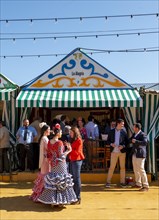 Spanish women with colorful flamenco dresses in front of marquees