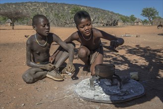 Children of the Ovahimba or Himba people look curiously into a pot over the fire