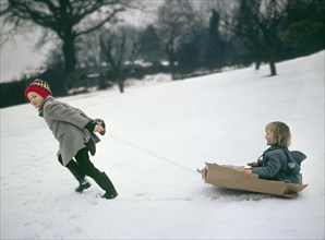 Two children ride on sledges made of cardboard