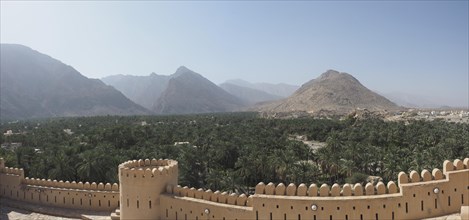 View over wall with battlements to palm oasis and Hajar Mountains