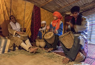 Bedouins with traditional clothes play on drums in a tent