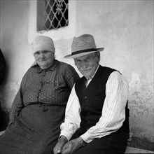 Old couple sitting on a bench and smiling at the camera