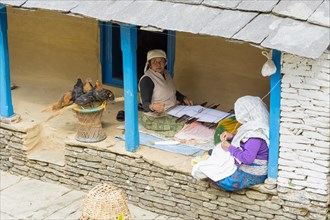 Two aged Nepalese women sitting in the doorway and sewing
