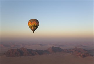 Hot-air balloon above an arid plain and isolated mountain ridges