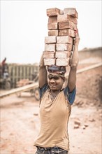 Worker with bricks on his head in the brickyard
