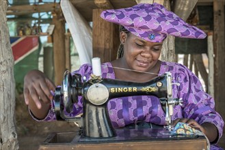 Native Herero woman with typical headgear and clothes is sitting at a sewing machine