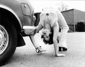 Woman looks under a car with flashlight