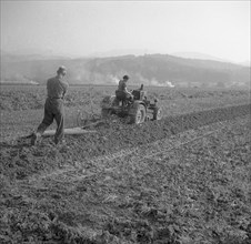 Workers plough the field with a tractor