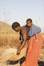 Tonga woman with child on her back sifting grains