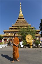 Buddhist monk stands in front of nine-story stupa Phra Mahathat Kaen Kakhon