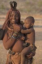 Young Himbafrau carries an infant on her arm