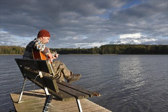 Man plays guitar on a boat landing stage at the lake
