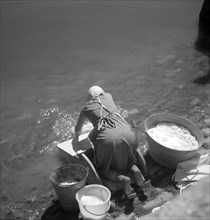 Woman washes her clothes in an old-fashioned way in the river around 1950