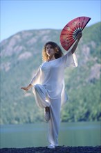 Young woman practicing Tai Chi with a red fan in a Crane