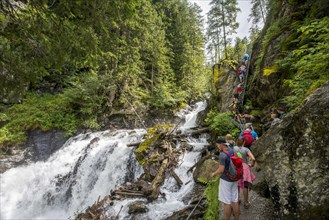 Hikers on the alpine path through the Hollschlucht gorge with waterfall