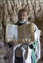 Orthodox priest of the rock church Mikael Mellehayzengi shows a book written by hand on parchment in the church language Ge'ez
