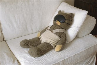 Teddy Bear lies with a sleeping mask on a couch