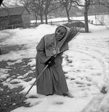 Witch with broom in hand stands in a curvilinear position in the snow
