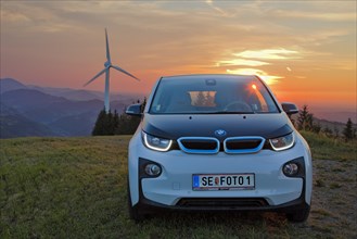 BMW electric car type i3 at the wind farm at sunset